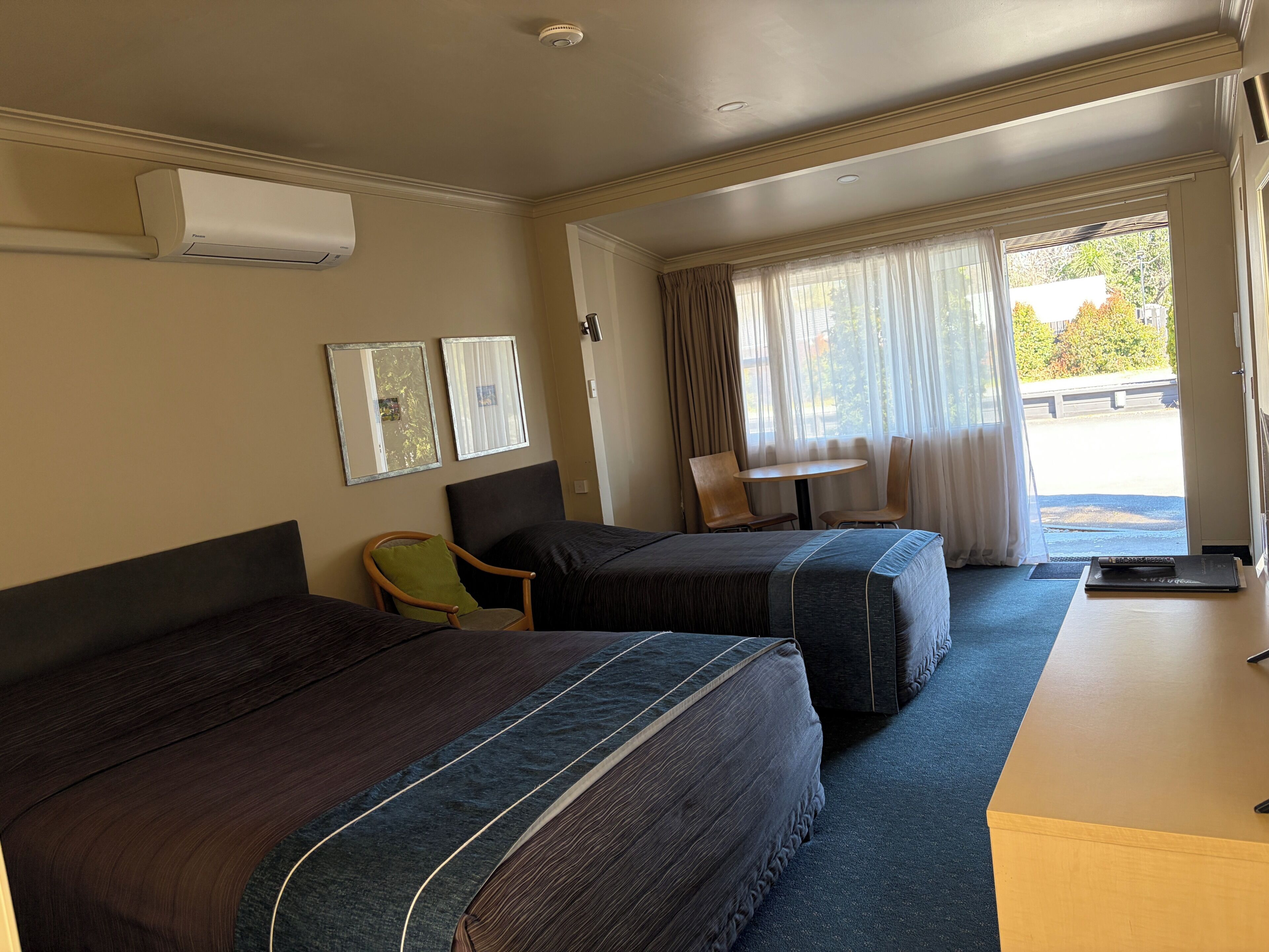 A hotel room with two beds, a small table, a chair, and a window with curtains.