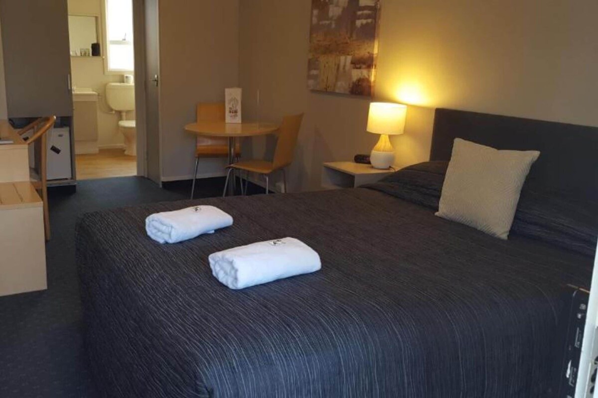 Une chambre d’hôtel avec un lit, un bureau, une chaise, une lampe et un tableau au mur.