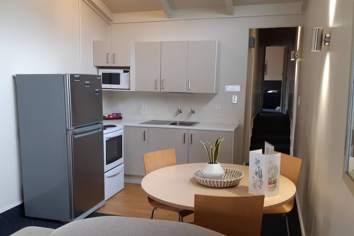 Cocina compacta con refrigerador, microondas, estufa y pileta. Hay una mesa de comedor con sillas y una pequeña planta.