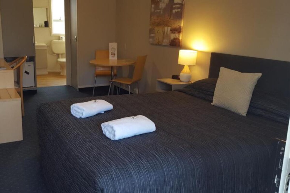 A hotel room with a large bed, a desk, and a chair.