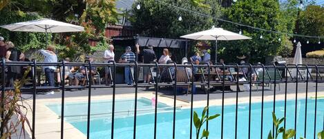 Une zone autour de la piscine, délimitée par une clôture, avec des parasols et des personnes présentes.