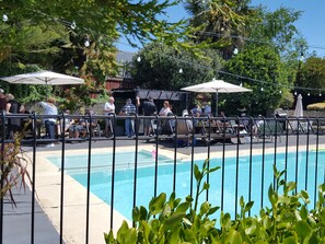 A pool area with a fence, umbrellas, and people around.