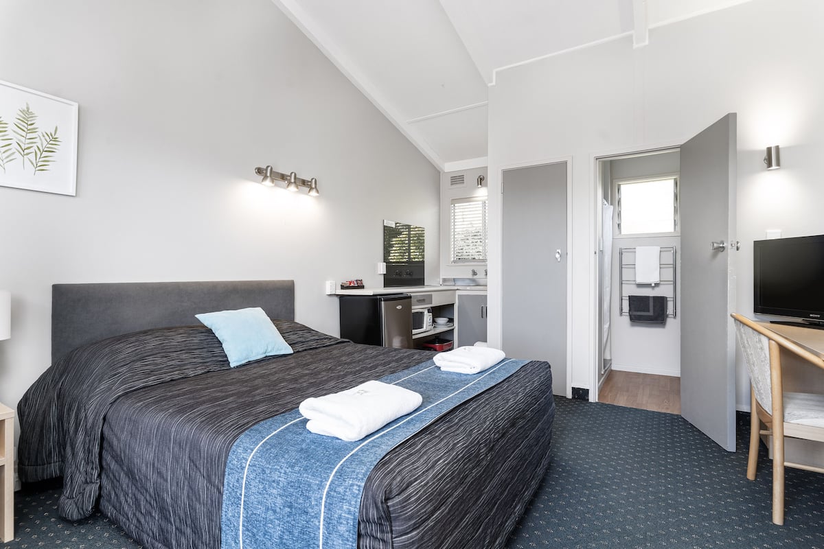 Habitación de hotel con una cama grande, un escritorio con computadora, televisor y baño visible a través de una puerta abierta.