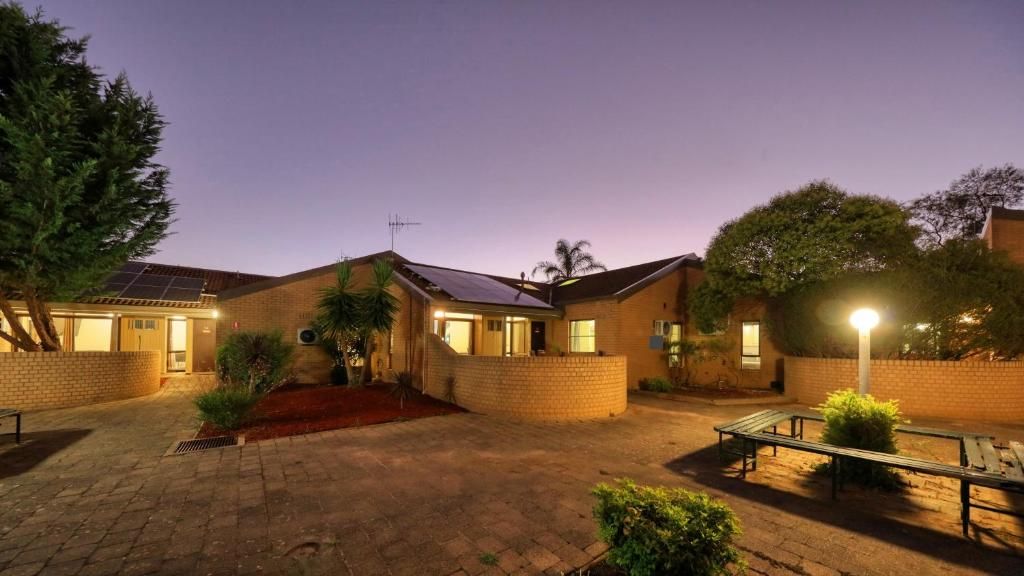 A residential building with a brick exterior, solar panels, and a paved courtyard with benches.