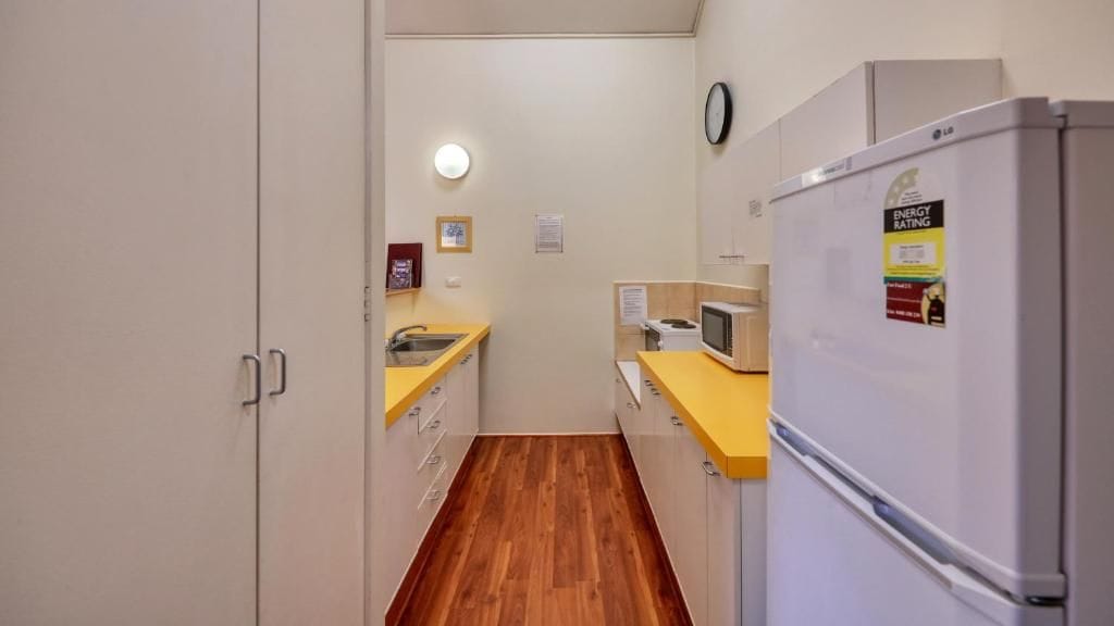 A compact kitchen with a microwave, refrigerator, sink, and wooden flooring.