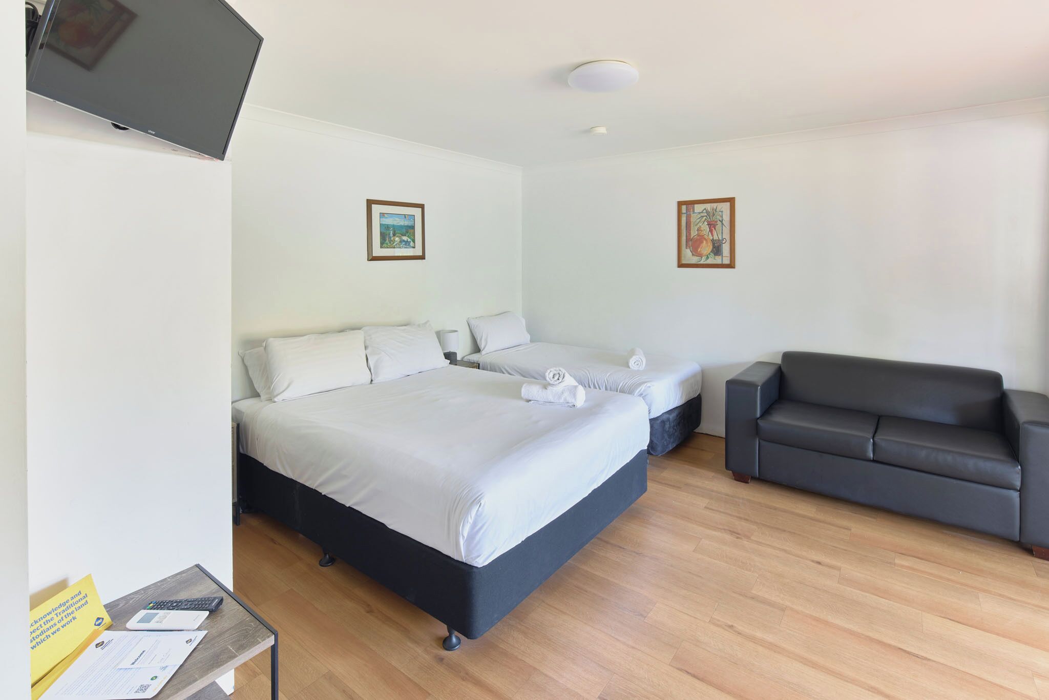 A bedroom with a bed, a sofa, a TV, and two framed pictures on the wall.