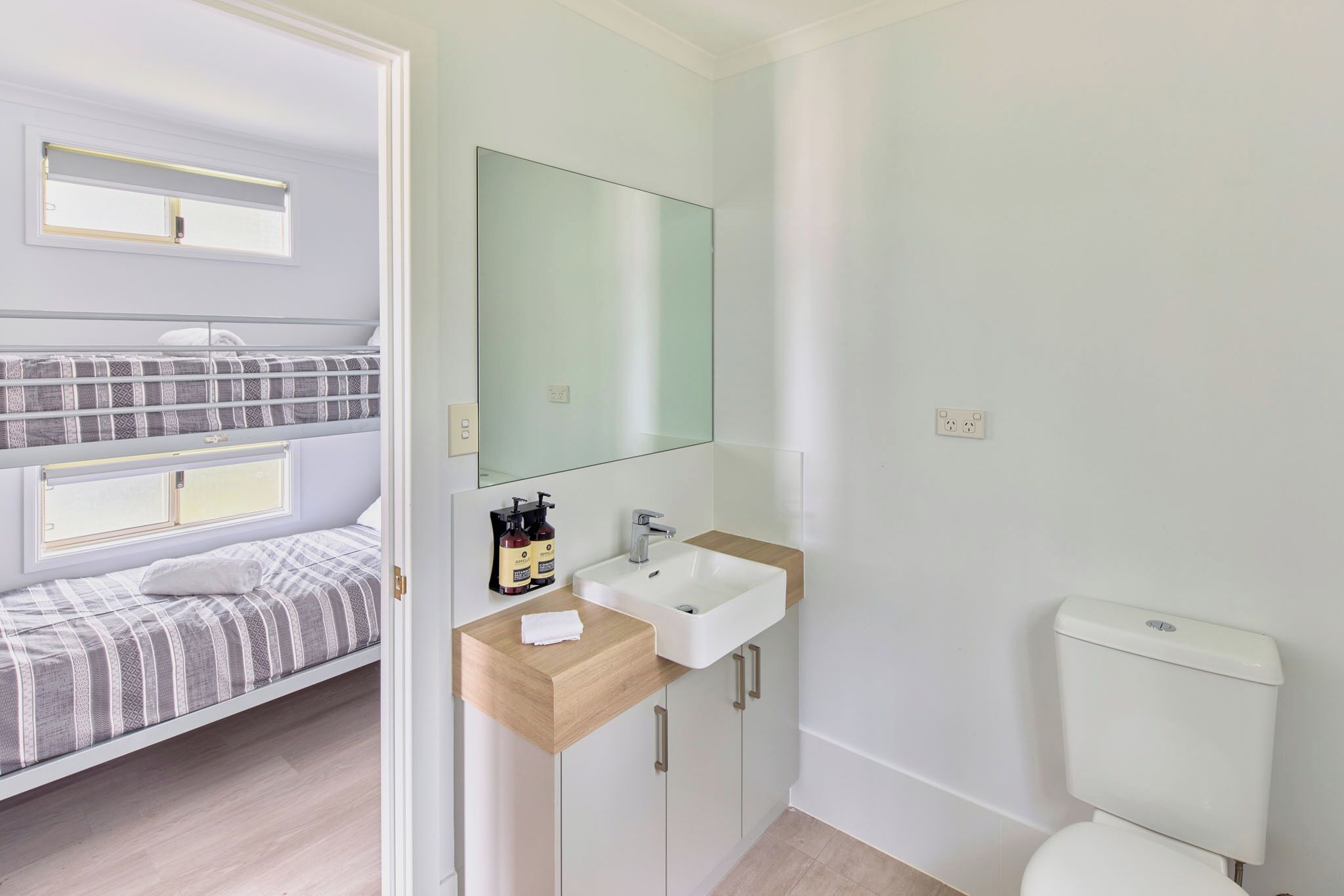 A modern bedroom with a bunk bed, a small sink, and a toilet.