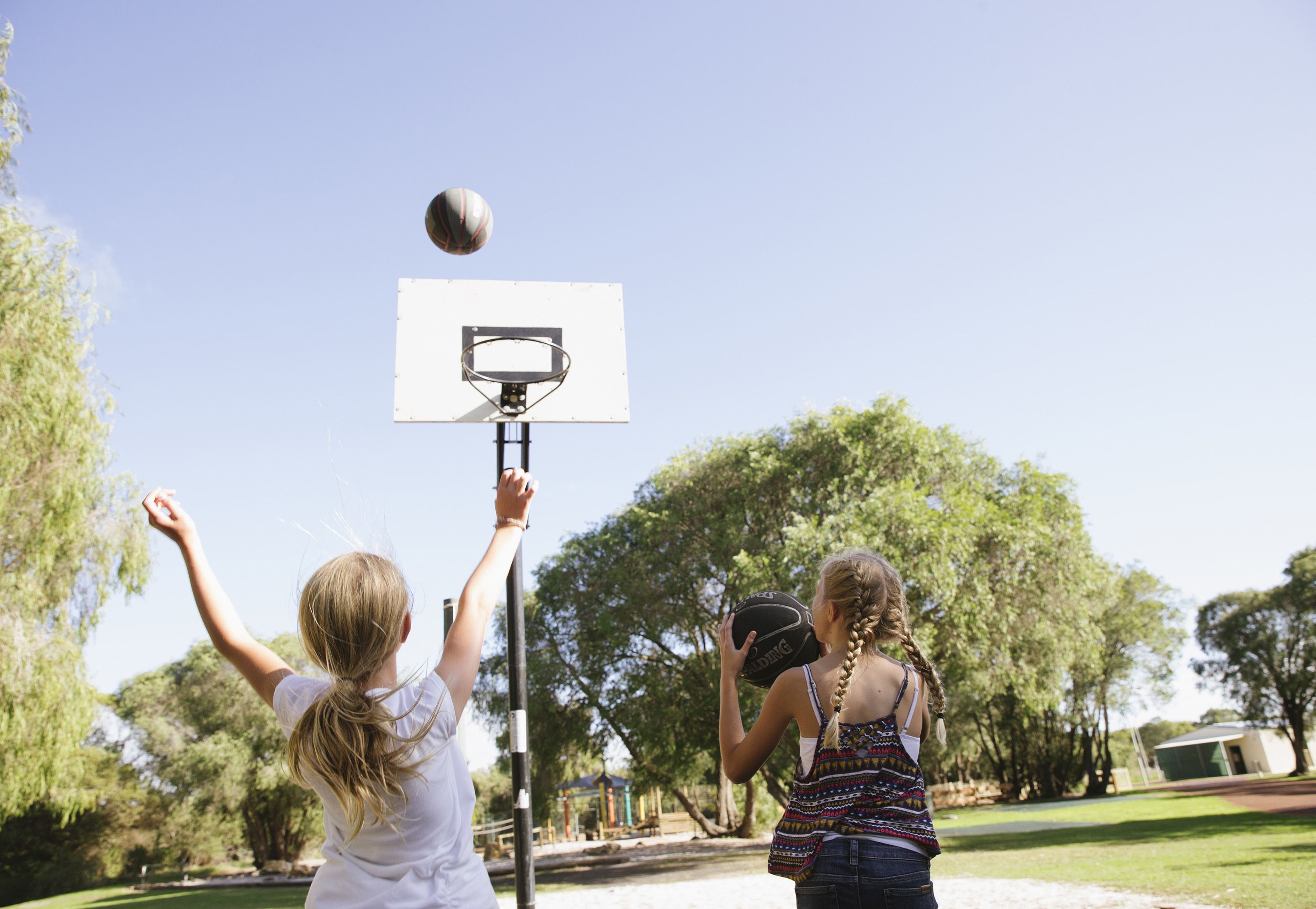 Två personer spelar basket i en park.