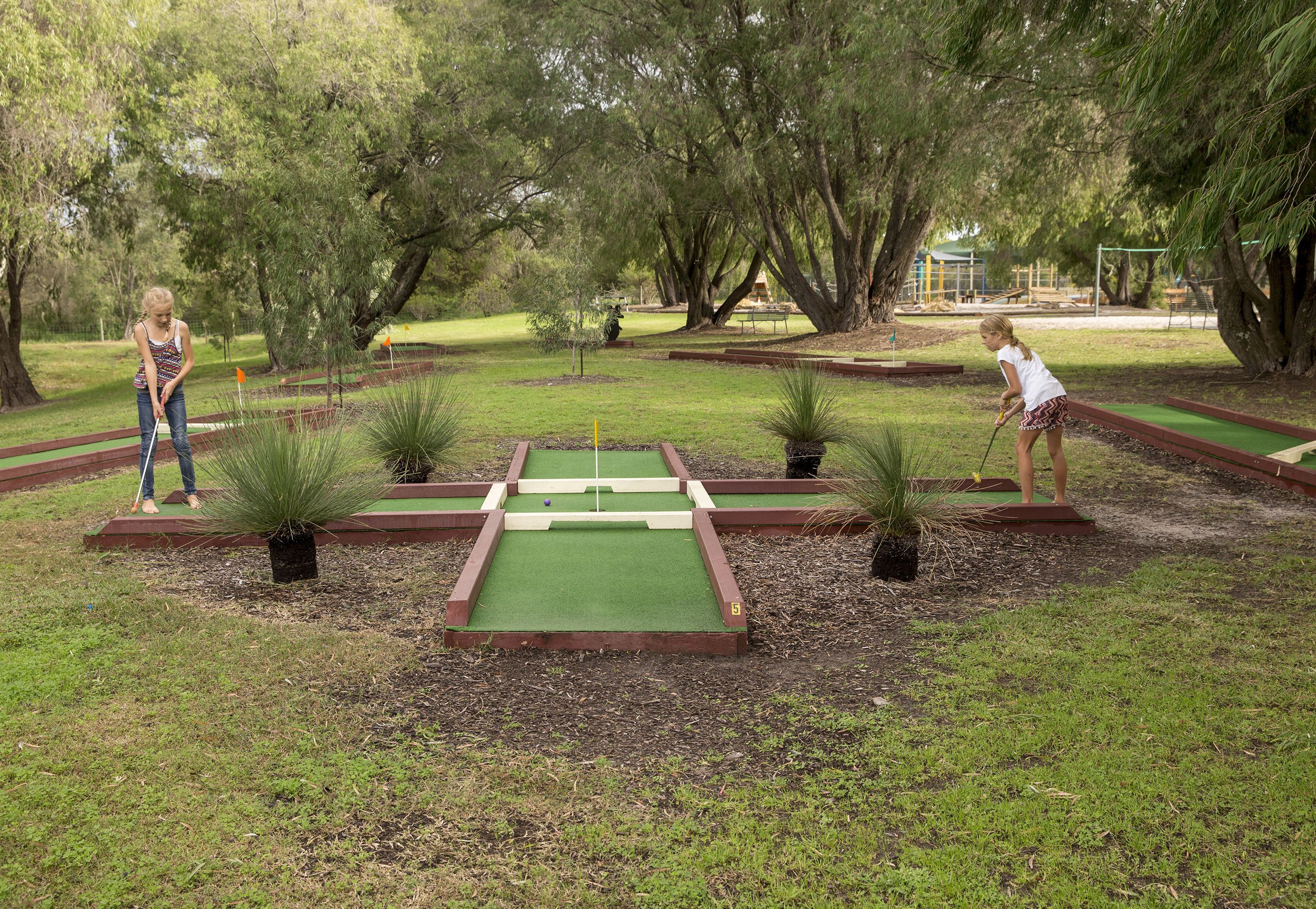 A miniature golf course with two players, surrounded by trees and greenery.