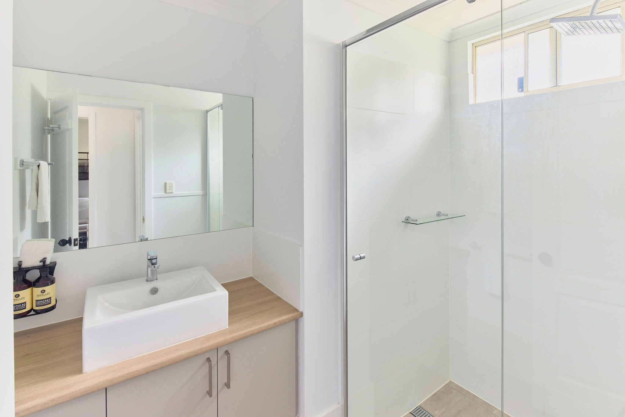 Ein modernes Badezimmer mit einem weißen Waschbecken, einer Duschkabine aus Glas und einem großen Spiegel.