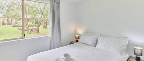 Habitación de hotel con una cama grande, una mesita de noche con lámpara, una ventana con vistas al exterior y un ventilador de techo.