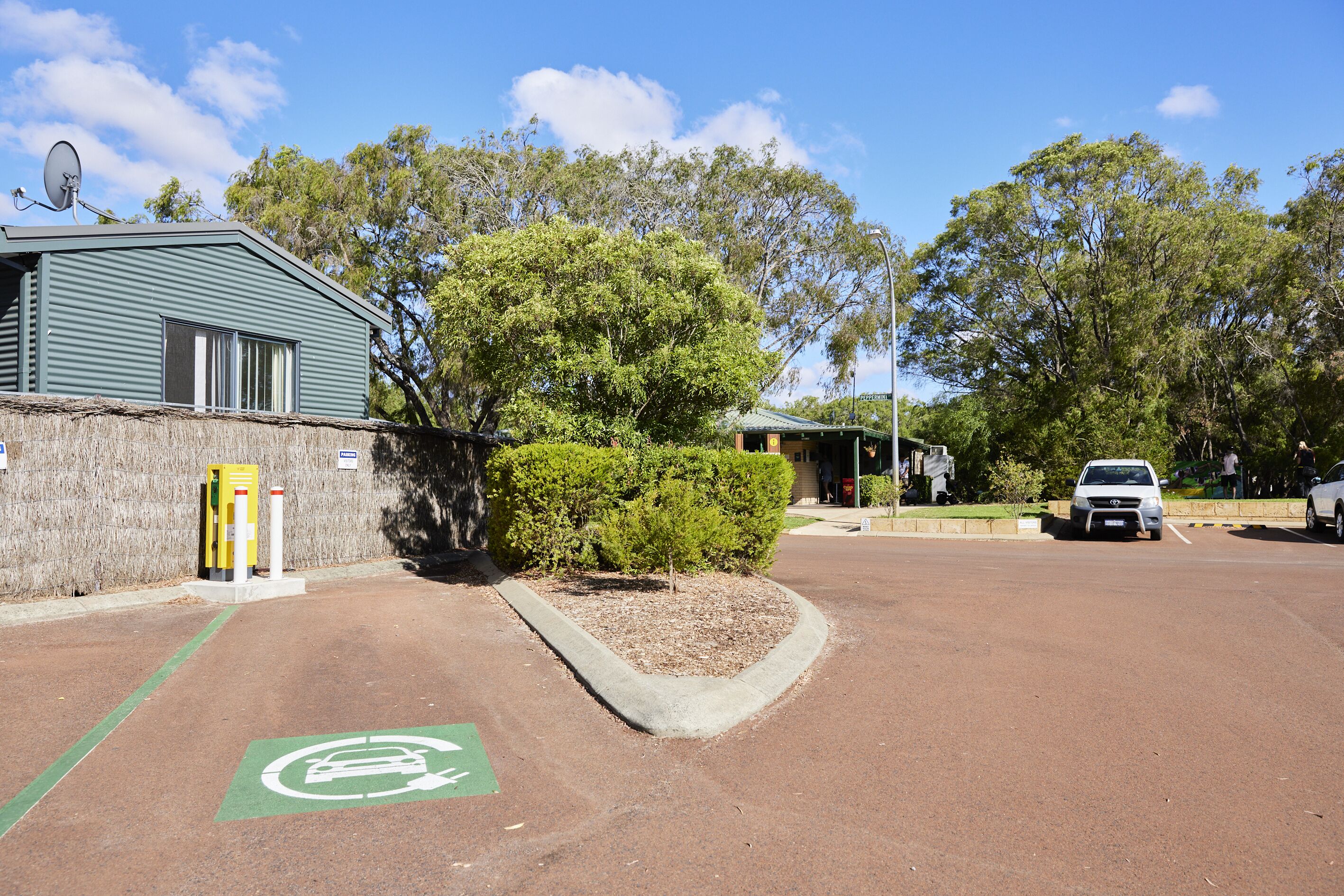 A parking area with a green bike lane, a building with a satellite dish, and a car in the background.