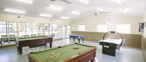 A pool room with multiple pool tables, ceiling fans, and large windows.