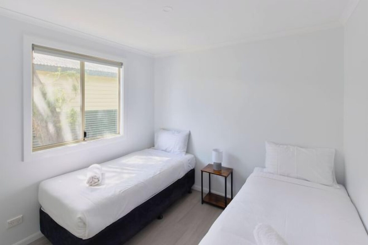 A room with two single beds, a small table, and a window with blinds.