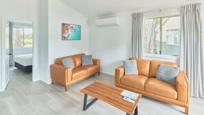 A modern living room with two leather sofas, a wooden coffee table, and a painting on the wall. - RAC Busselton Holiday Park (Abbey)