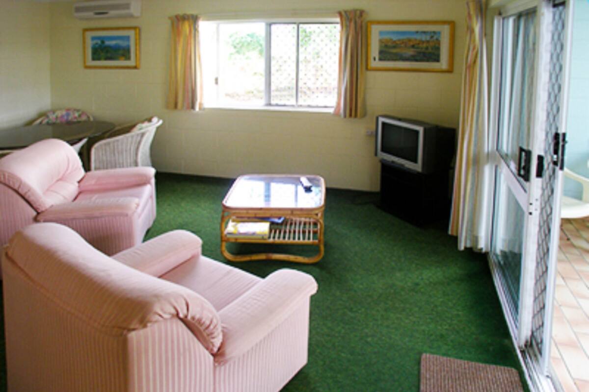 A living room with a green carpet, two pink sofas, a wicker coffee table, a television, and a window with curtains.