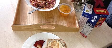 A breakfast tray with cereal, toast, a cup of coffee, a bottle of milk, and a vase with flowers.