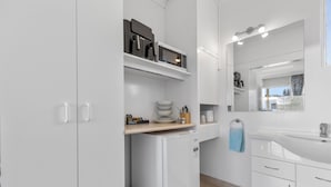 Una cocina moderna con armarios blancos, microondas integrado, cafetera y lavabo con espejo arriba.