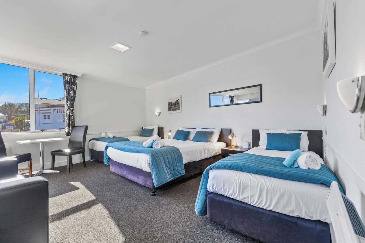 A hotel room with three beds, a desk, and a chair.