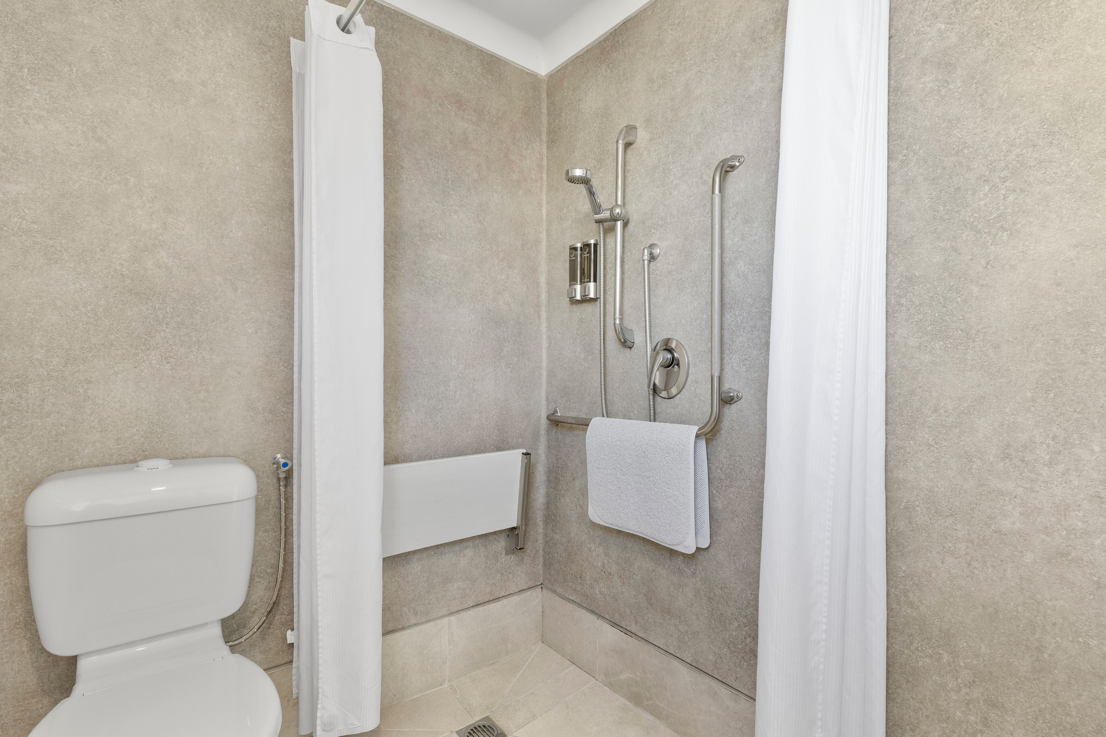 Un baño moderno con ducha, inodoro y barras de apoyo.