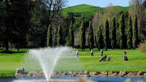 Un campo de golf con una fuente, árboles y un paisaje montañoso al fondo.