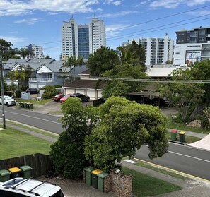 A residential street with houses, parked cars, and tall buildings in the background. - Saltwater Villas (Mooloolaba)