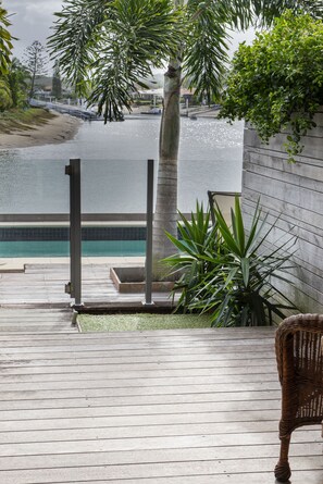 A wooden deck with a view of a swimming pool and a palm tree. - Saltwater Villas (Mooloolaba)