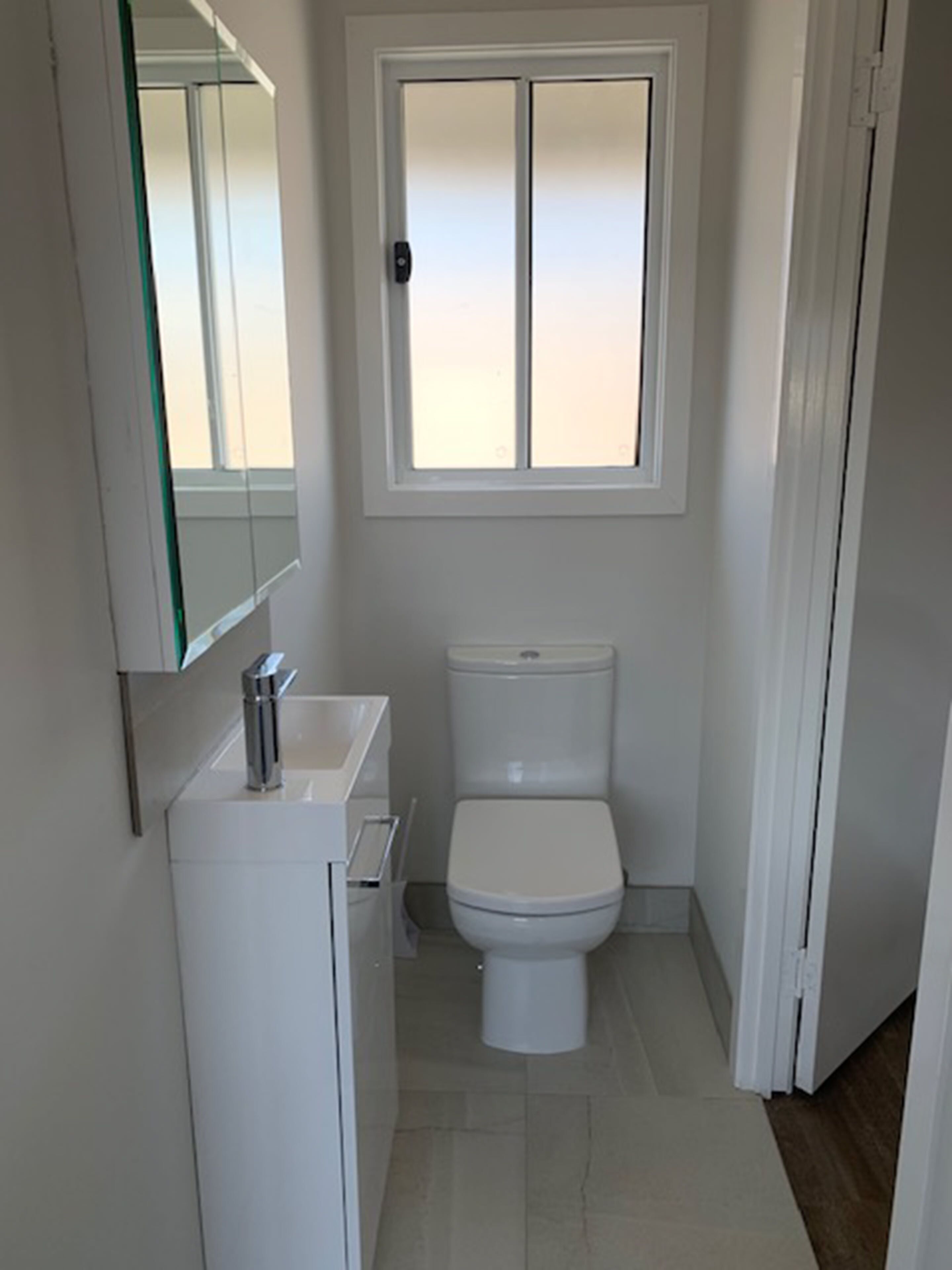 A compact bathroom with a toilet, a sink, and a mirror.