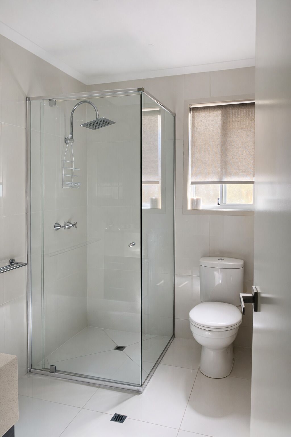 Ein modernes Badezimmer mit einer gläsernen Duschkabine, einer Toilette und einem Fenster mit Vorhang.