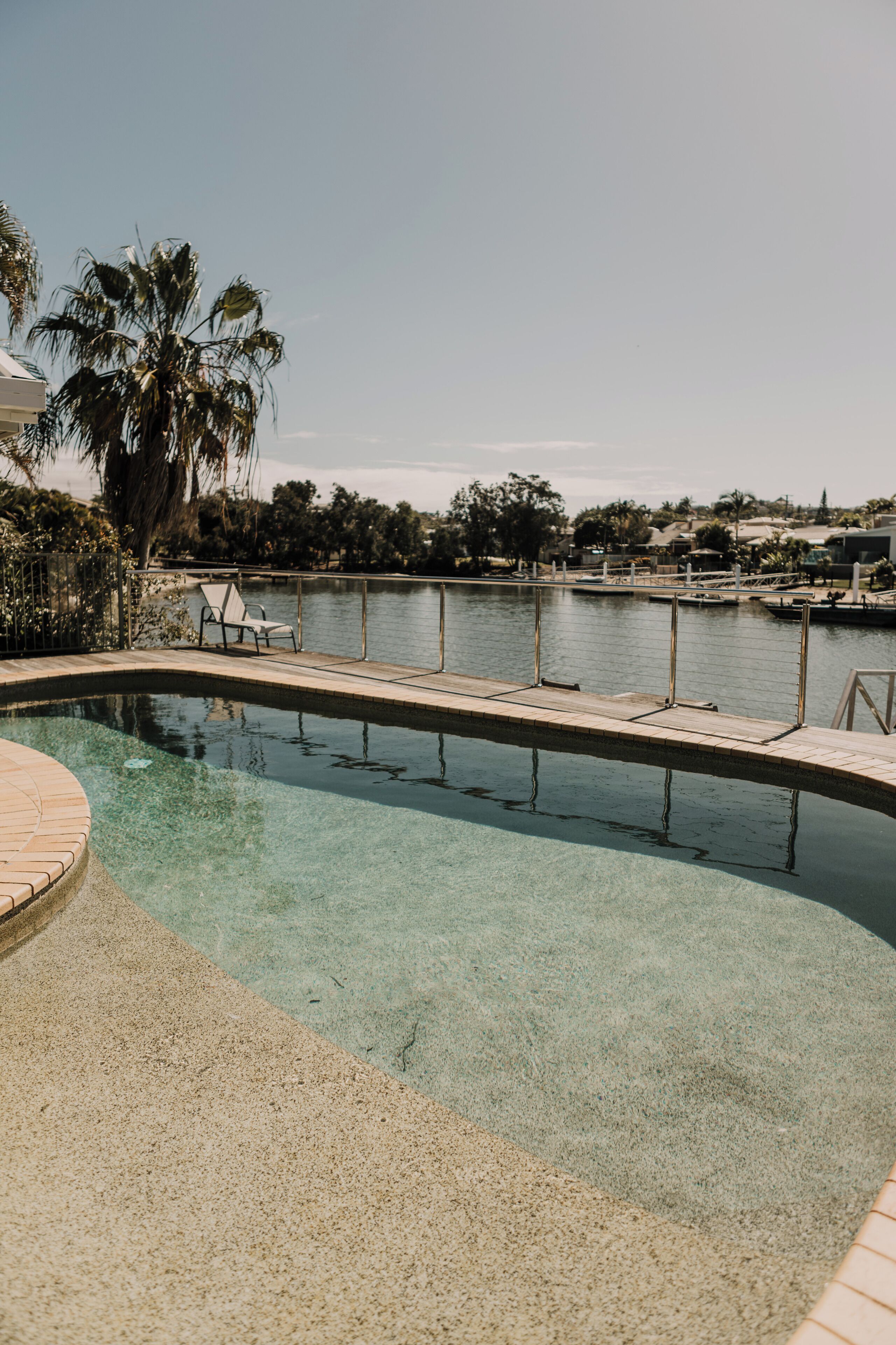 A swimming pool with clear water, a wooden deck, and a view of a body of water and distant buildings.