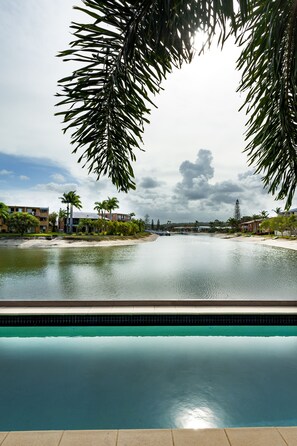 A pool with a clear view of a river and buildings in the background. - Saltwater Villas (Mooloolaba)