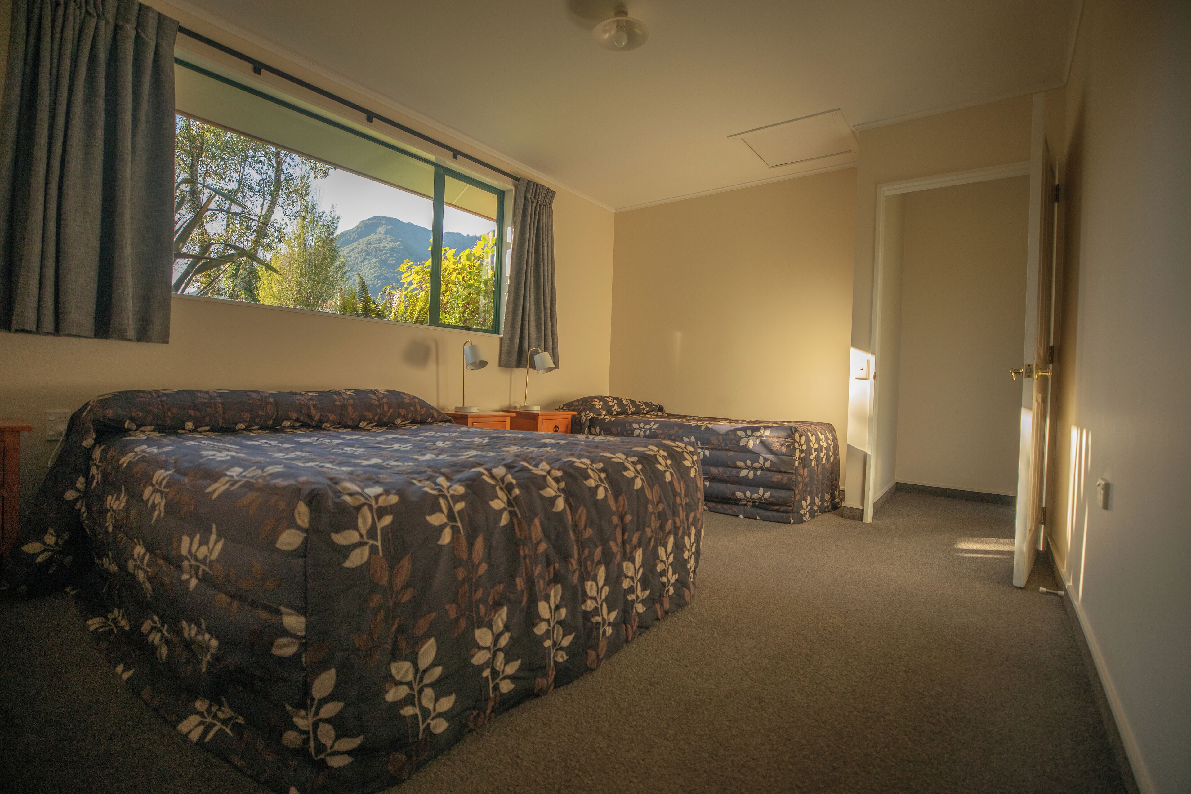 A bedroom with a large bed, a smaller bed, a window with curtains, and a door.