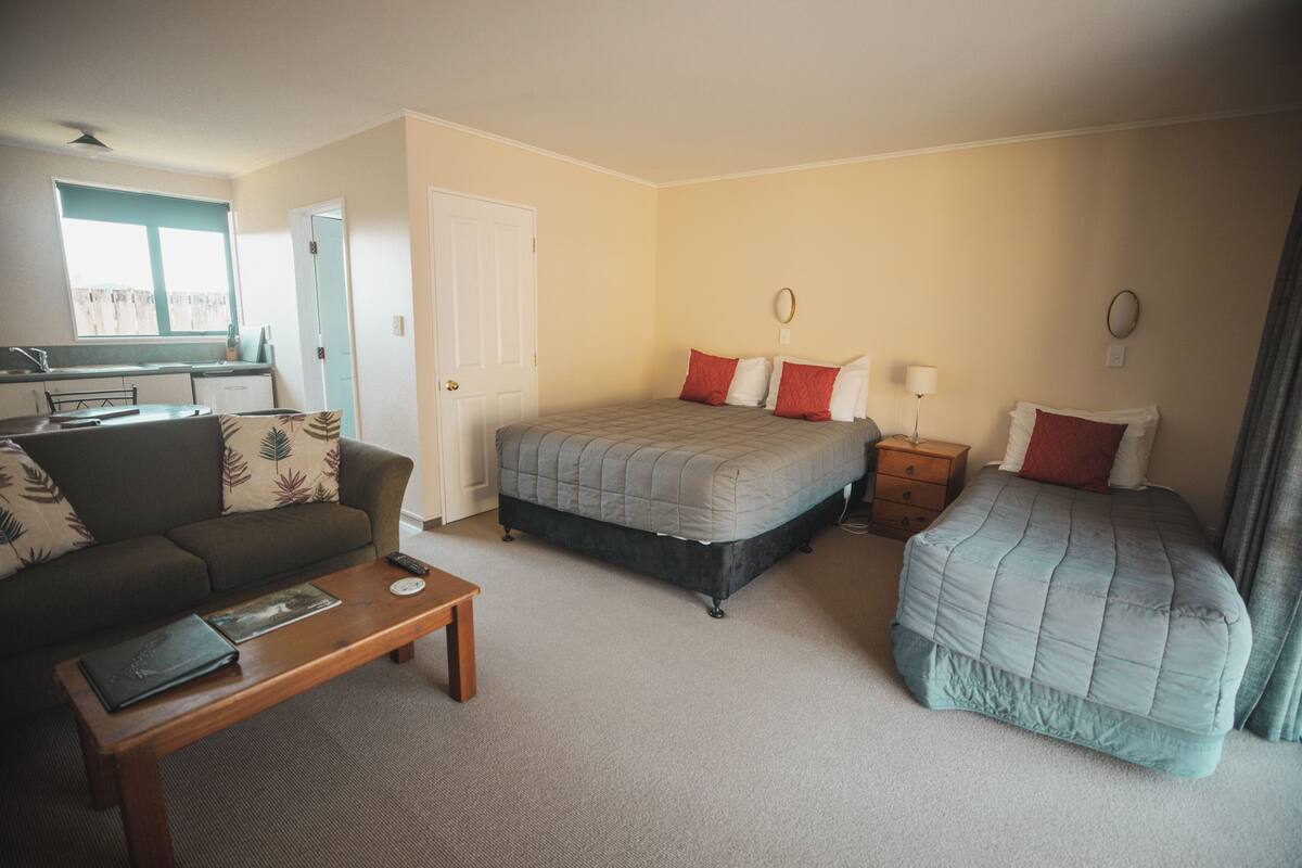 A bedroom with a bed, a sofa, a bedside table, and a window.