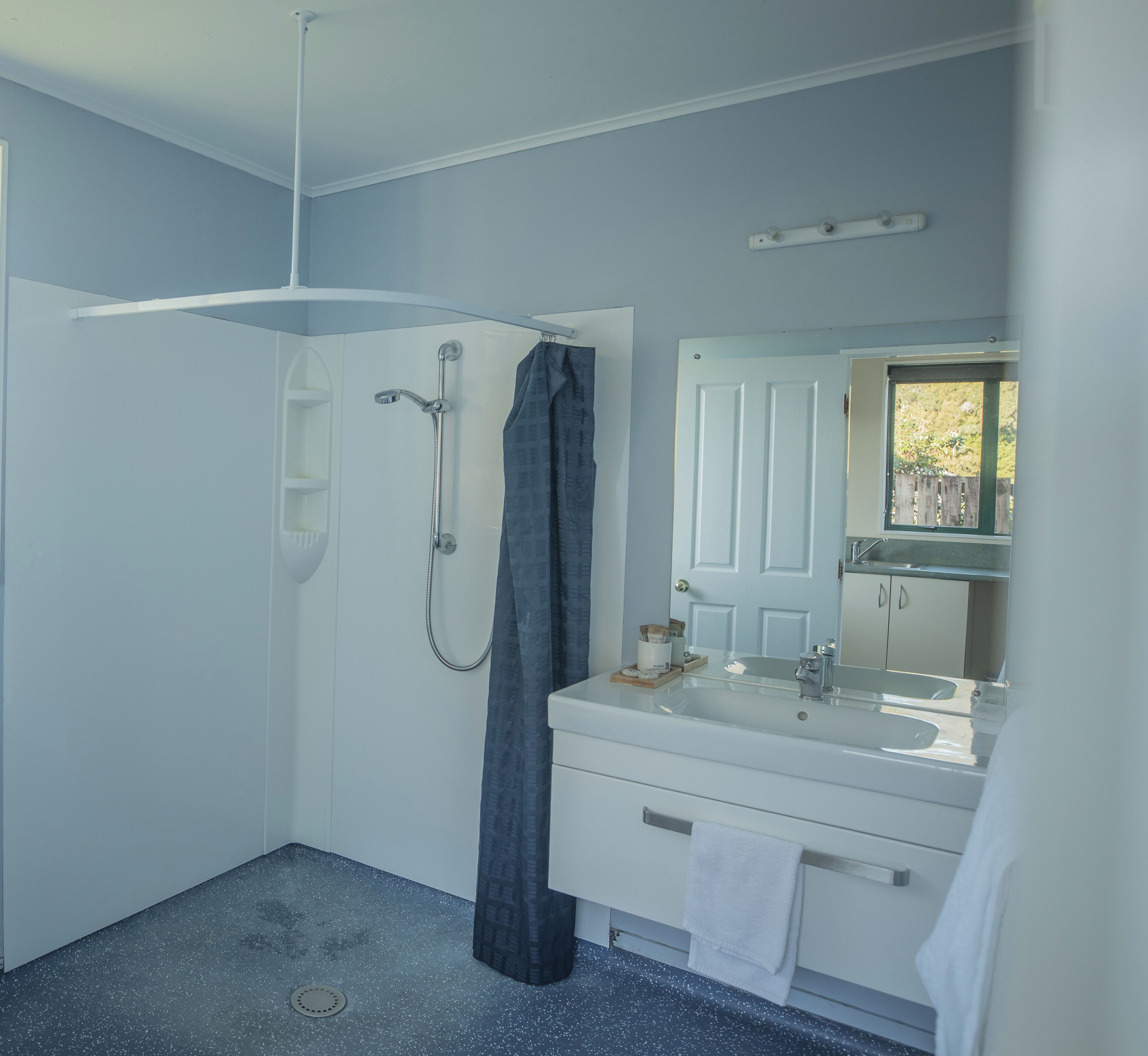 A bathroom with a shower, a sink, a mirror, and a window.