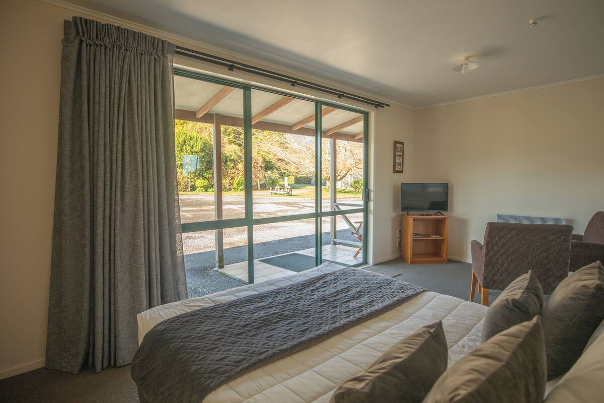 A hotel room with a bed, a TV, a seating area with chairs, and a view of the outdoors.