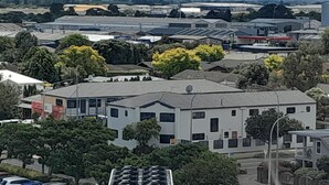 A modern building with a flat roof, surrounded by greenery and parked cars. - Abode Motel (Palmerston North)