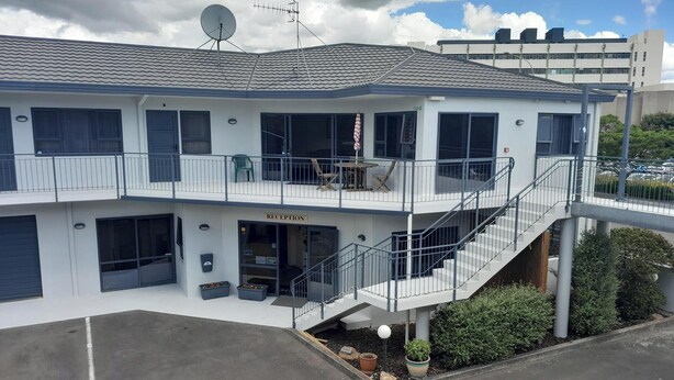 A two-story building with a reception area, outdoor seating, and a staircase leading to the upper floor. - Abode Motel (Palmerston North)
