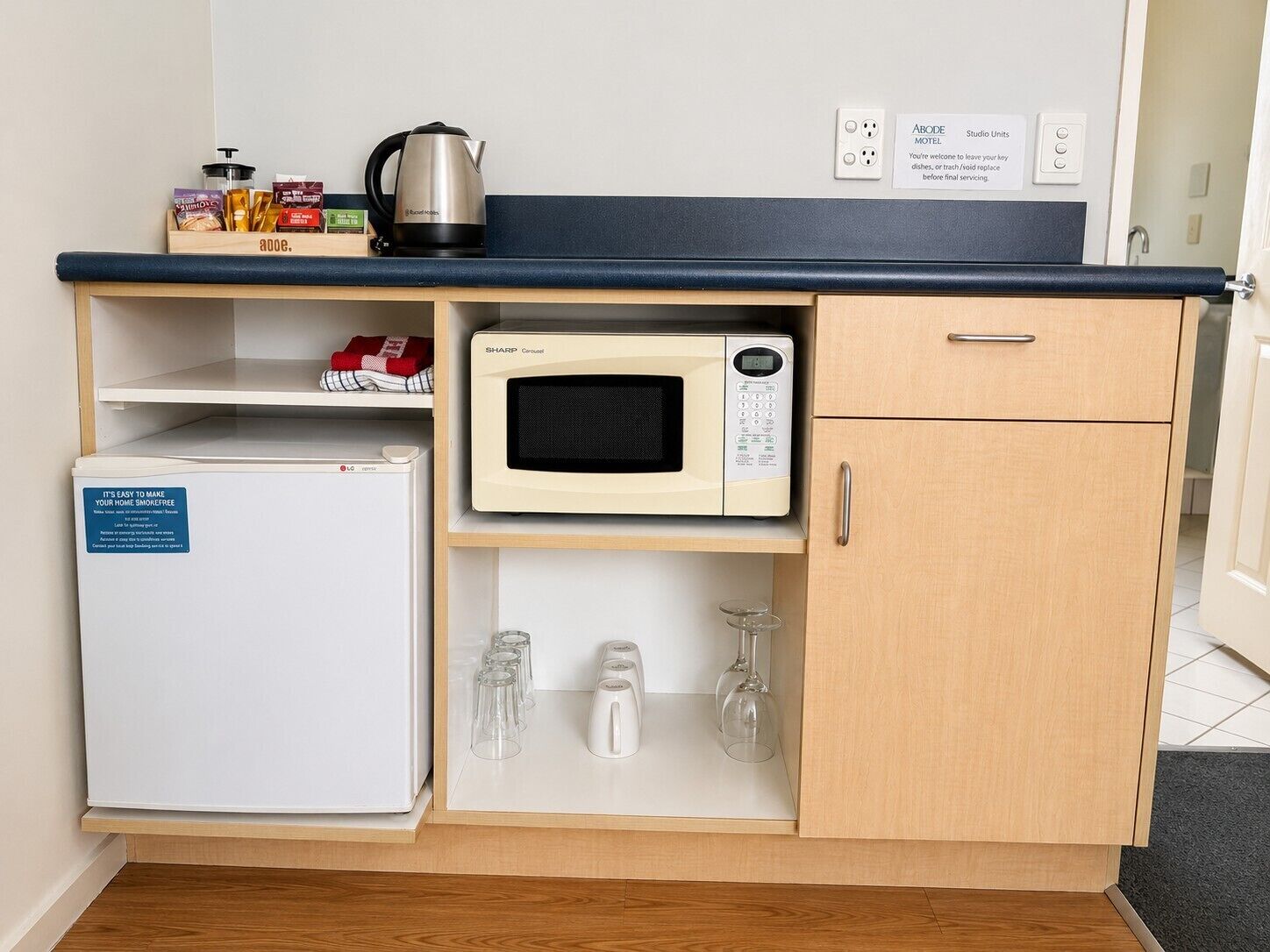 Een kitchenette met een magnetron, een kleine koelkast, een waterkoker en een koffiezetapparaat.