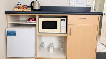Een kitchenette met een magnetron, een kleine koelkast, een waterkoker en een koffiezetapparaat.