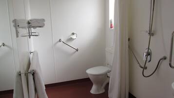 Et badeværelse med toilet, bruser med håndbruser og gelænder.