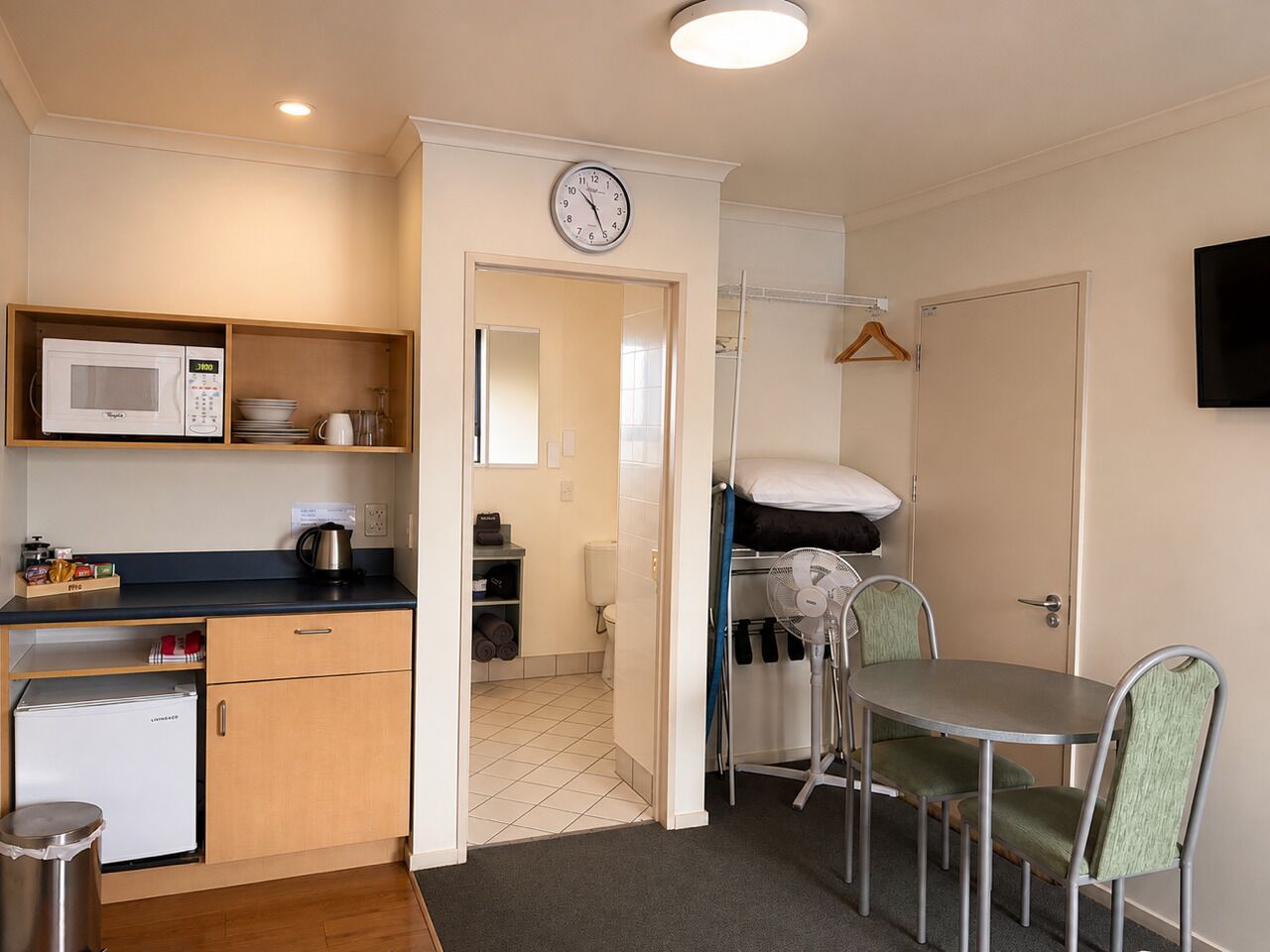 A compact kitchen with a microwave, sink, and a small refrigerator. There is a dining area with a table and chairs.