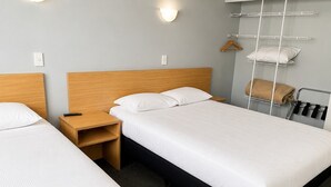 Habitación de hotel con dos camas individuales, una mesita de noche de madera, un estante en la pared con una toalla y un perchero.