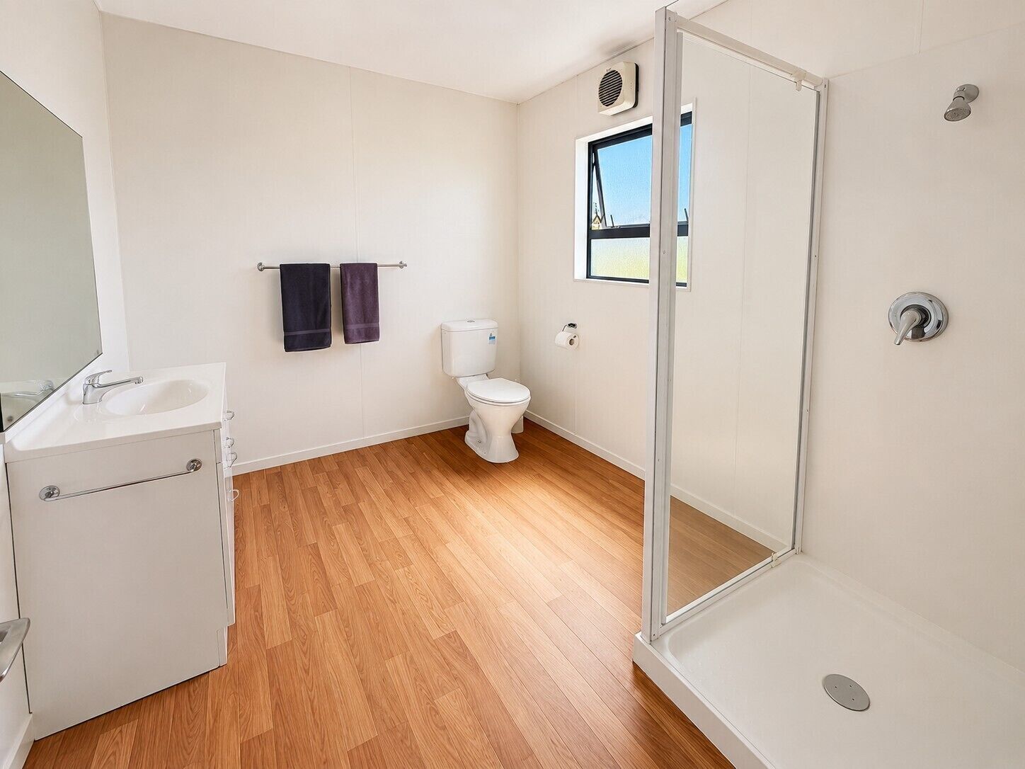 A bathroom with a shower, toilet, sink, and a window.