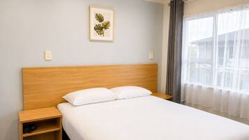 A hotel room with a wooden headboard, a single bed with white bedding, a nightstand, and a framed plant on the wall.