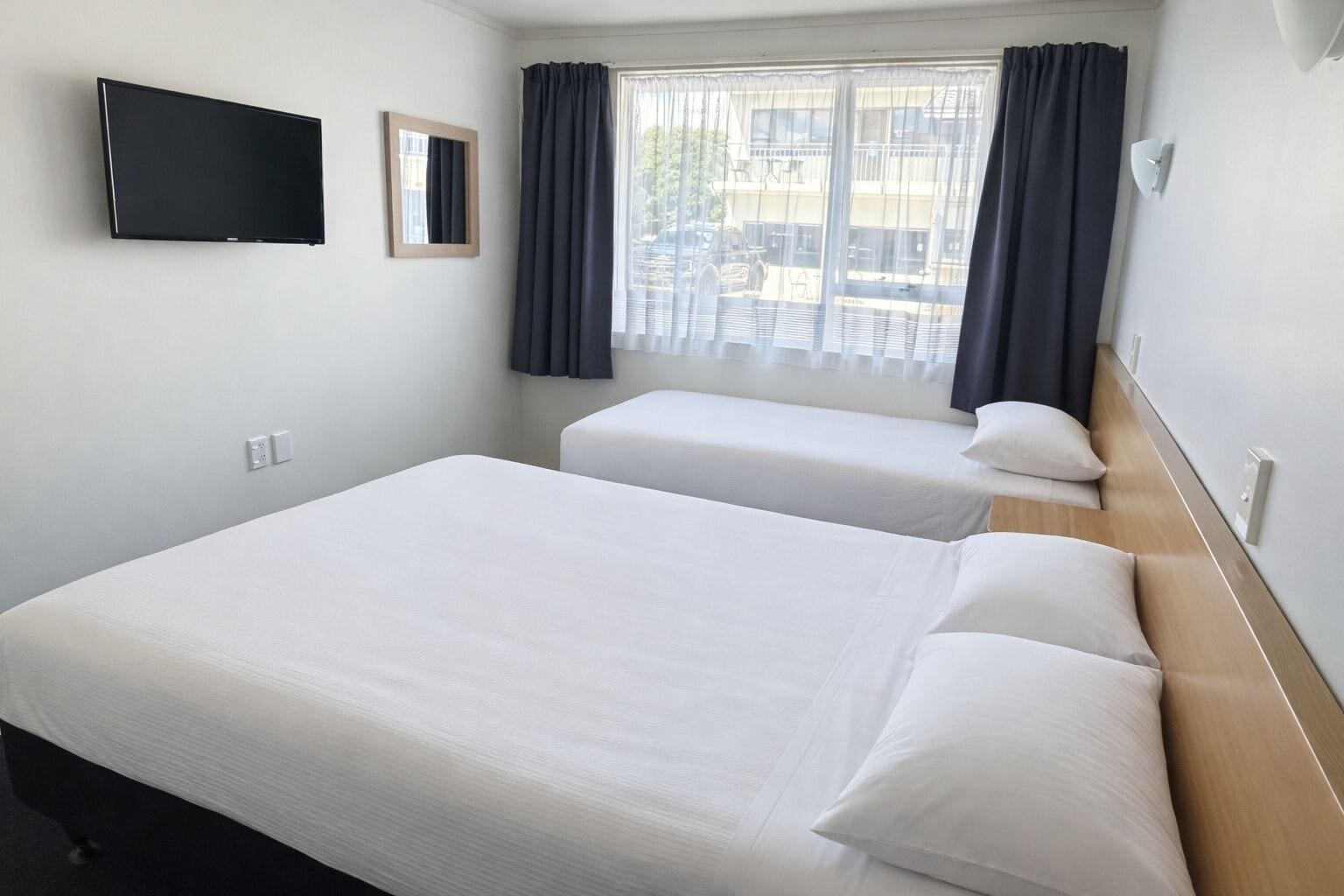 Habitación de hotel con dos camas, televisión y ventana con cortinas.