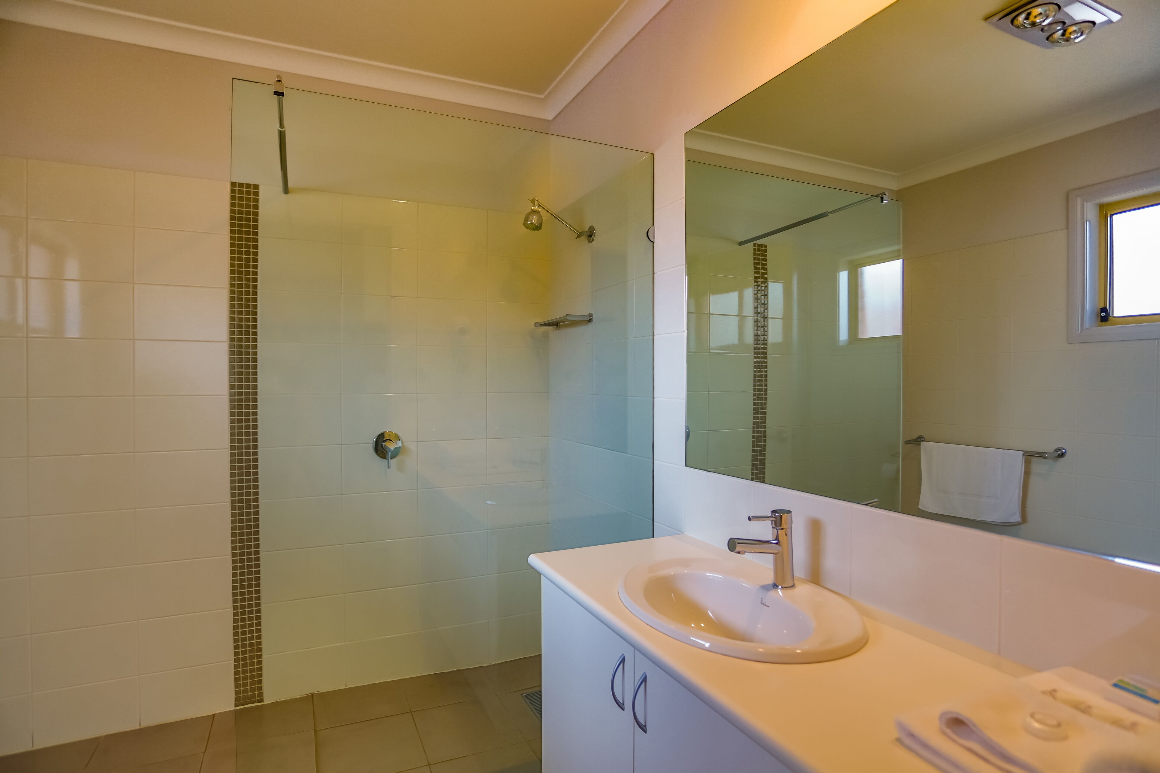 Un bany modern amb un envàs de dutxa de vidre, un lavabo blanc i un mirall gran.