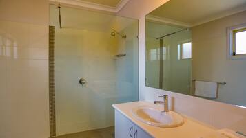 Un bany modern amb un envàs de dutxa de vidre, un lavabo blanc i un mirall gran.