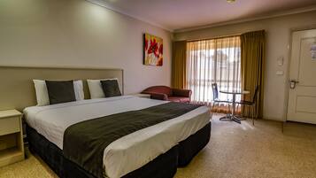 Una habitación de hotel con una cama grande, un escritorio, una silla y un ventanal con cortinas.
