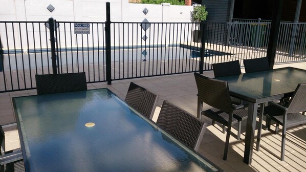 Ett utomhusområde med en pool, bord och stolar, en stängd grind och en skylt som visar var poolområdet ligger.