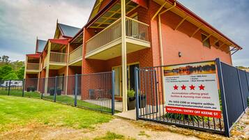 A two-story motel with a red brick facade, a balcony on the second floor, and a sign advertising standard rooms, a pool, BBQ area, and a view of the Murray Waters.